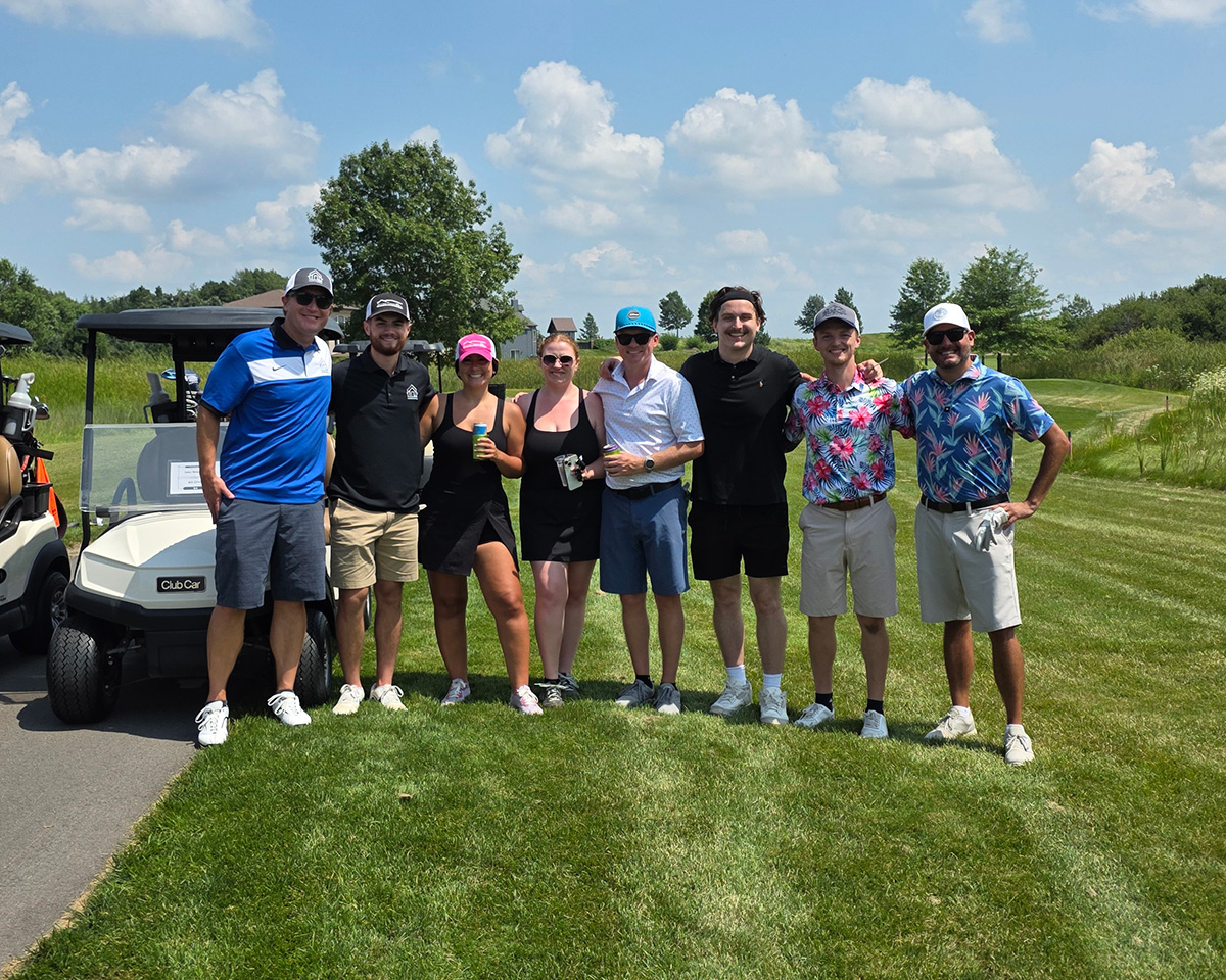Adults in golf attire pose for a photo on a golf course next to a golf cart.